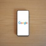 A smartphone displaying the Google homepage on a wooden surface, viewed from above.