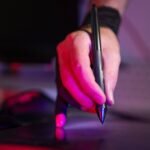 A digital artist's hand working on a graphics tablet with a stylus, in a creative studio setting.